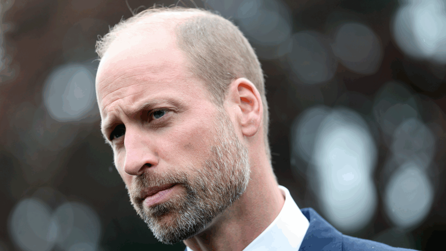 Prince William Isn’t Going to Hide From “Emotional Problems” as King Like Monarchs of the Past, Says Royal Biographer Prince William wearing a white shirt and blue jacket looking stern