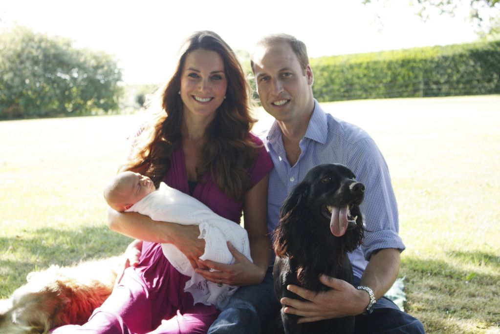 Princess Kate, Prince William, a baby Prince George in Kate's arms and Lupo the dog sat in the grass together