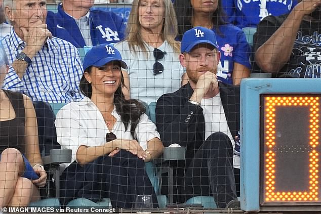 Meghan sat court-side at a World Series Baseball game with Prince Harry opting for an effortlessly chic ensemble of a crisp white Givenchy shirt, previously worn at the Endeavour Fund Awards, Veronica Beard jeans and a baseball hat