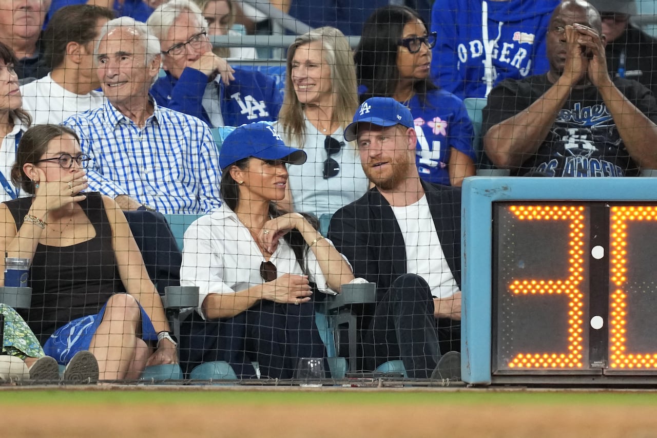 People sit in the front row of a baseball stadium behind a net.
