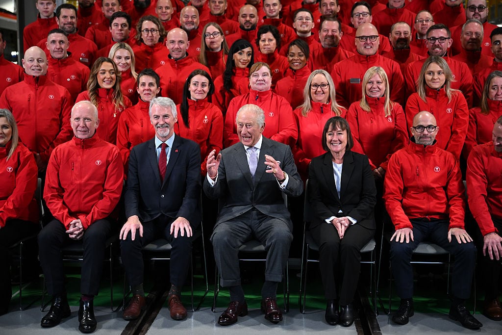 Several people sit in rows. Many are wearing red jackets.