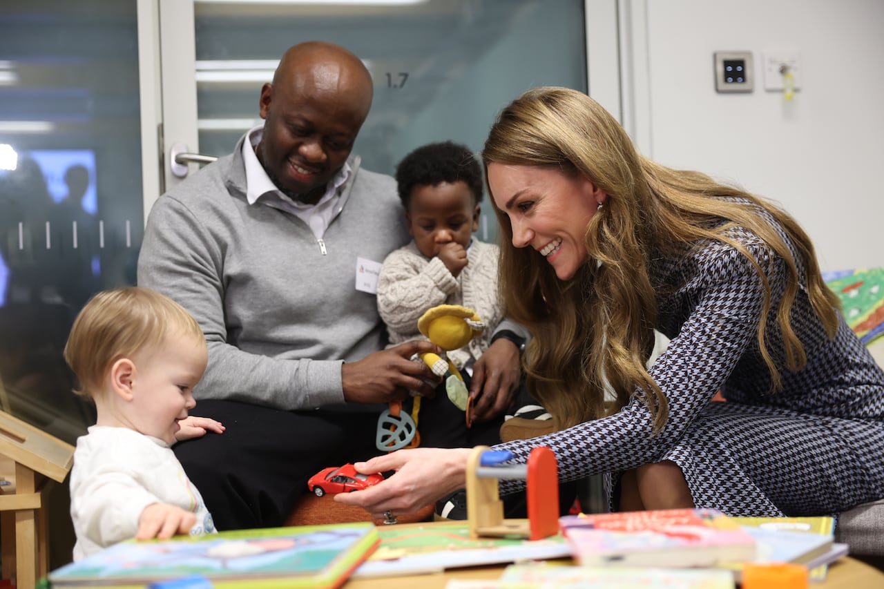 An adult holds out a toy car to a child while other adults and children are nearby.