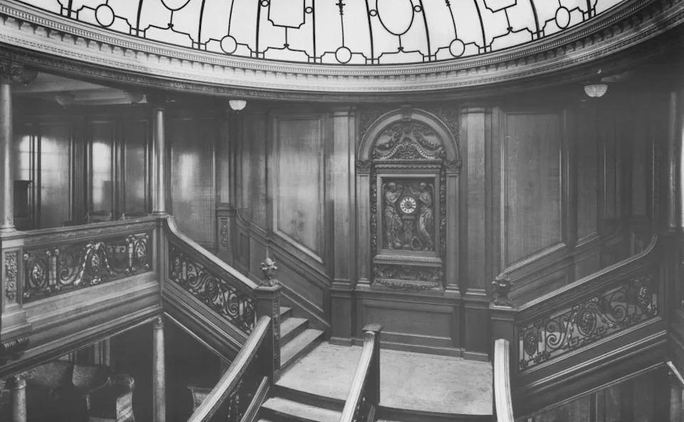 Historic grand staircase with intricate woodwork and ornate railings under a decorative glass dome ceiling