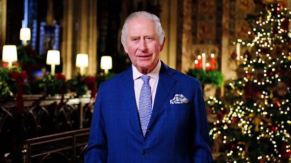 King Charles wearing a blue suit in front of a Christmas tree