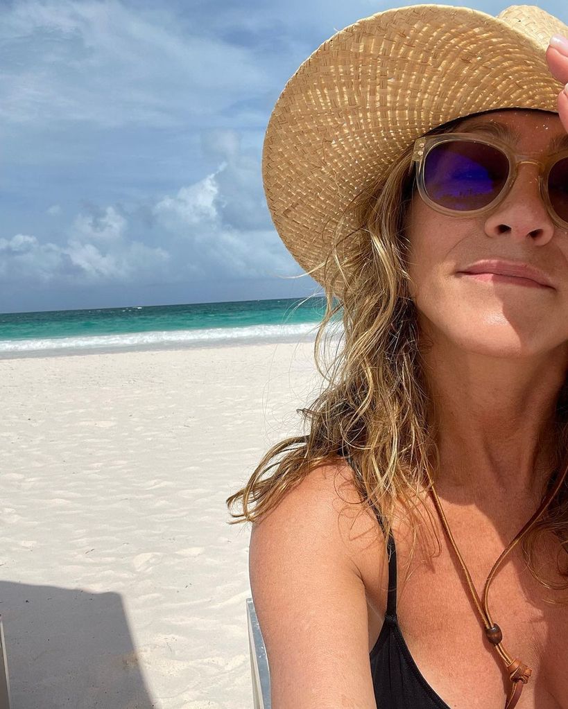 Jennifer Anniston in swimwear and straw hat posing on beach