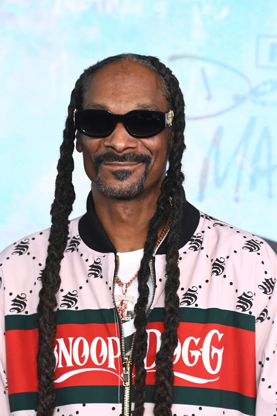 Person with long braids and sunglasses, wearing a patterned jacket with the name "Snoop Dogg" on the front