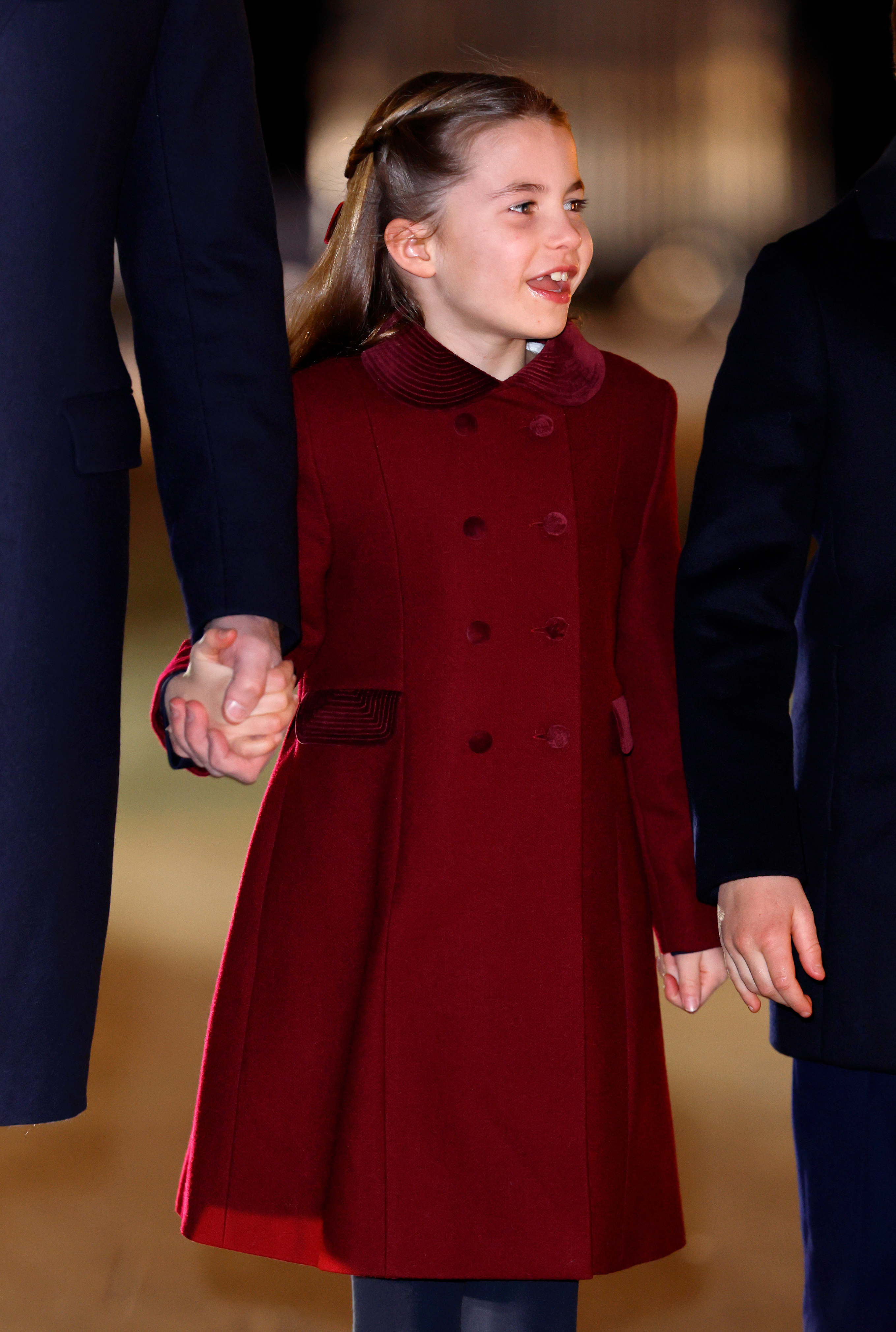 Princess Charlotte wearing a burgundy coat and smiling holding Prince William's hand
