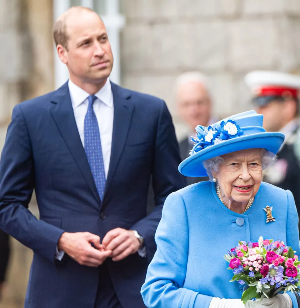  Prince William wearing a blue suit walking behind Queen Elizabeth, dressed in light blue. 