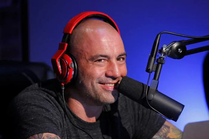 Person wearing headphones speaks into a microphone, smiling, in a podcast studio setting