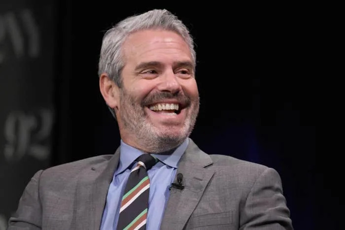 Andy Cohen in a suit with a striped tie, sitting on stage during an event or interview