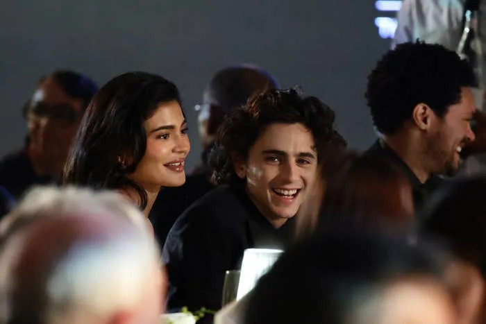 Kylie Jenner and Timothée Chalamet sitting at a table, smiling and engaged in conversation at an event