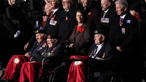 PA Media Three World War Two veterans, wearing medals and berets, are pushed along Whitehall in wheelchairs