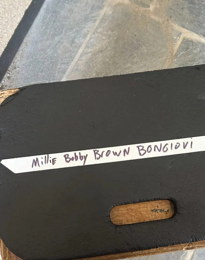 A black chair back with a label reading "Millie Bobby Brown Bongiovi" in handwritten text