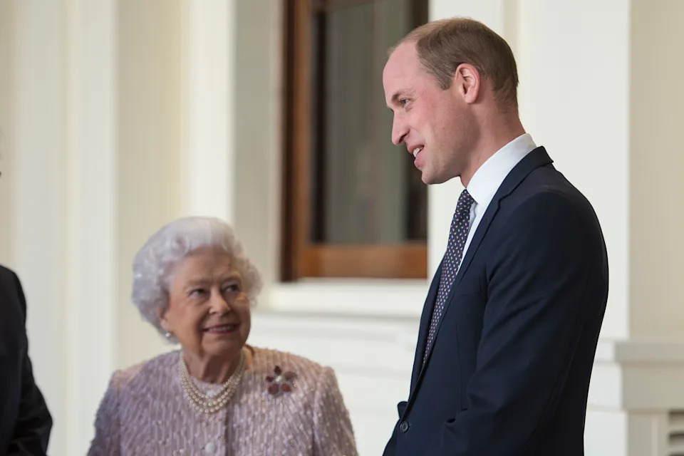 Queen Elizabeth standing next to Prince William, looking up at him smiling 