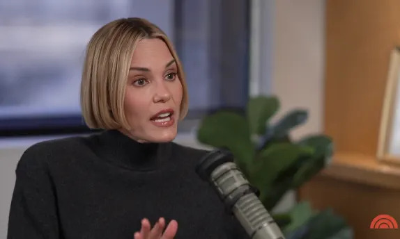 Person with a short bob hairstyle speaking into a microphone during an interview, wearing a turtleneck