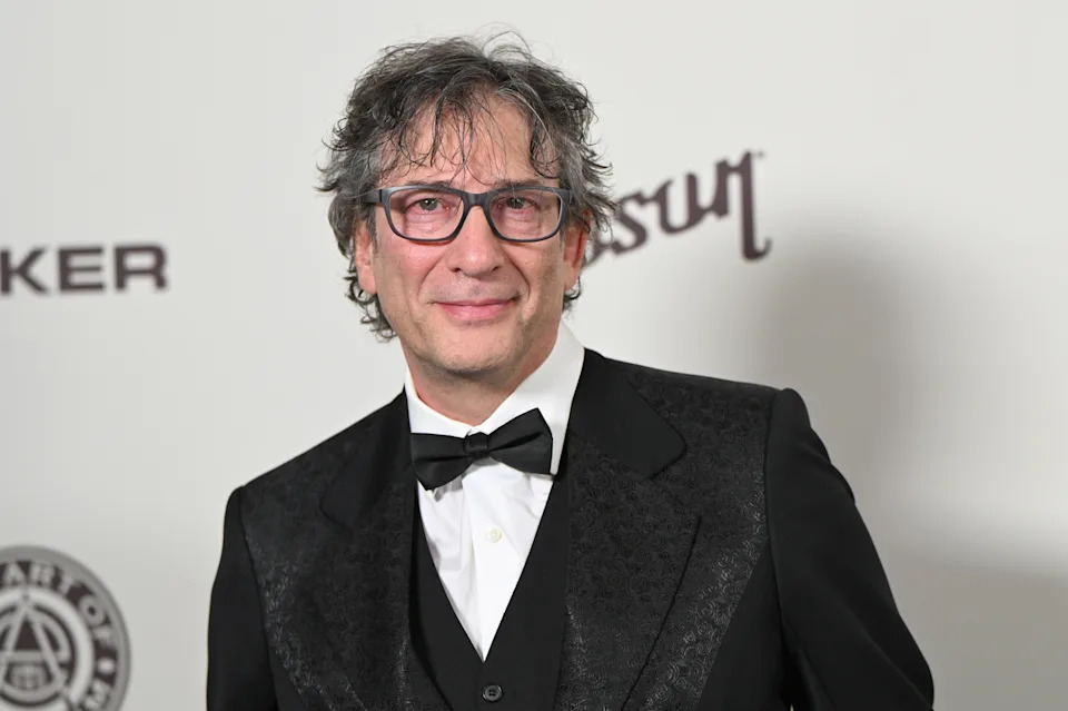 Person in a tailored tuxedo and bowtie on a red carpet at a formal event, smiling at the camera