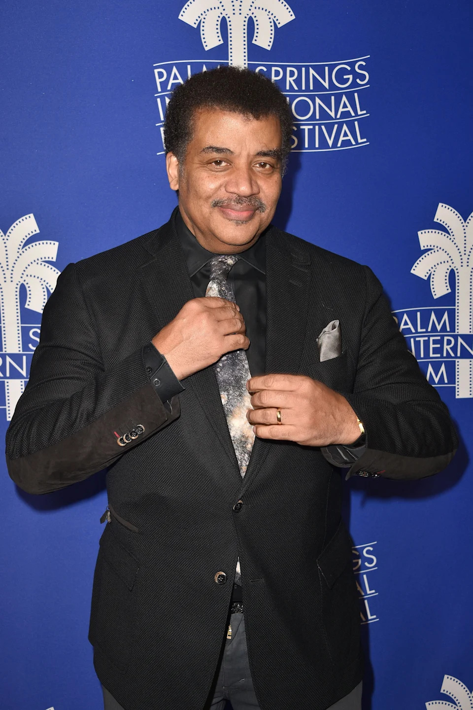 Person in a formal suit adjusting their tie at the Palm Springs International Film Festival