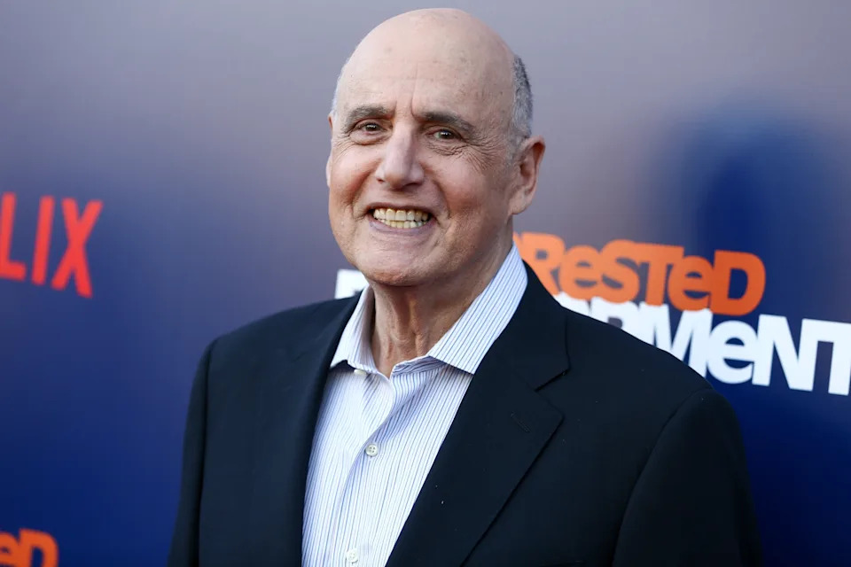 A person in a suit and striped shirt smiles at a Netflix event backdrop