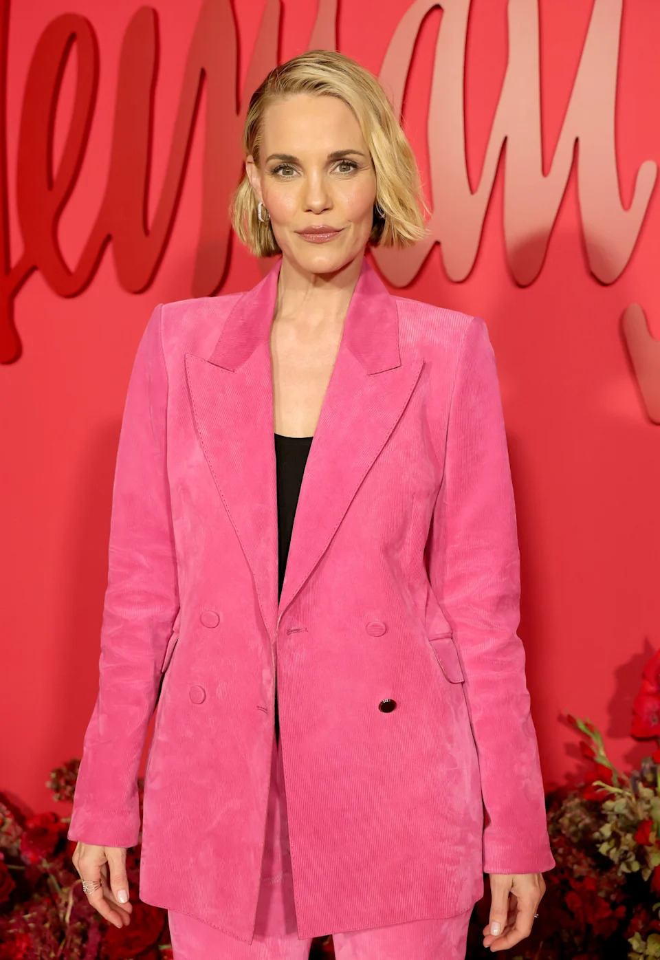 A woman on the red carpet wears a chic pink suit with a black top. Wavy, short hair completes her elegant look