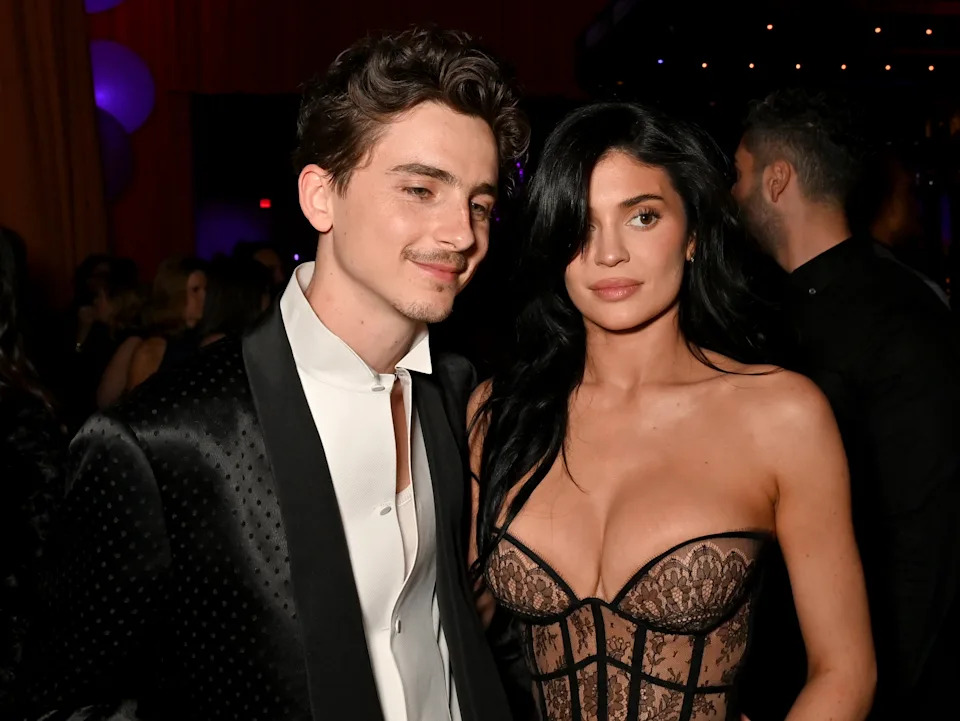 Timothée Chalamet and Kylie Jenner pose together at an event. The man wears a tailored black suit, and the woman is in an elegant corset-style dress