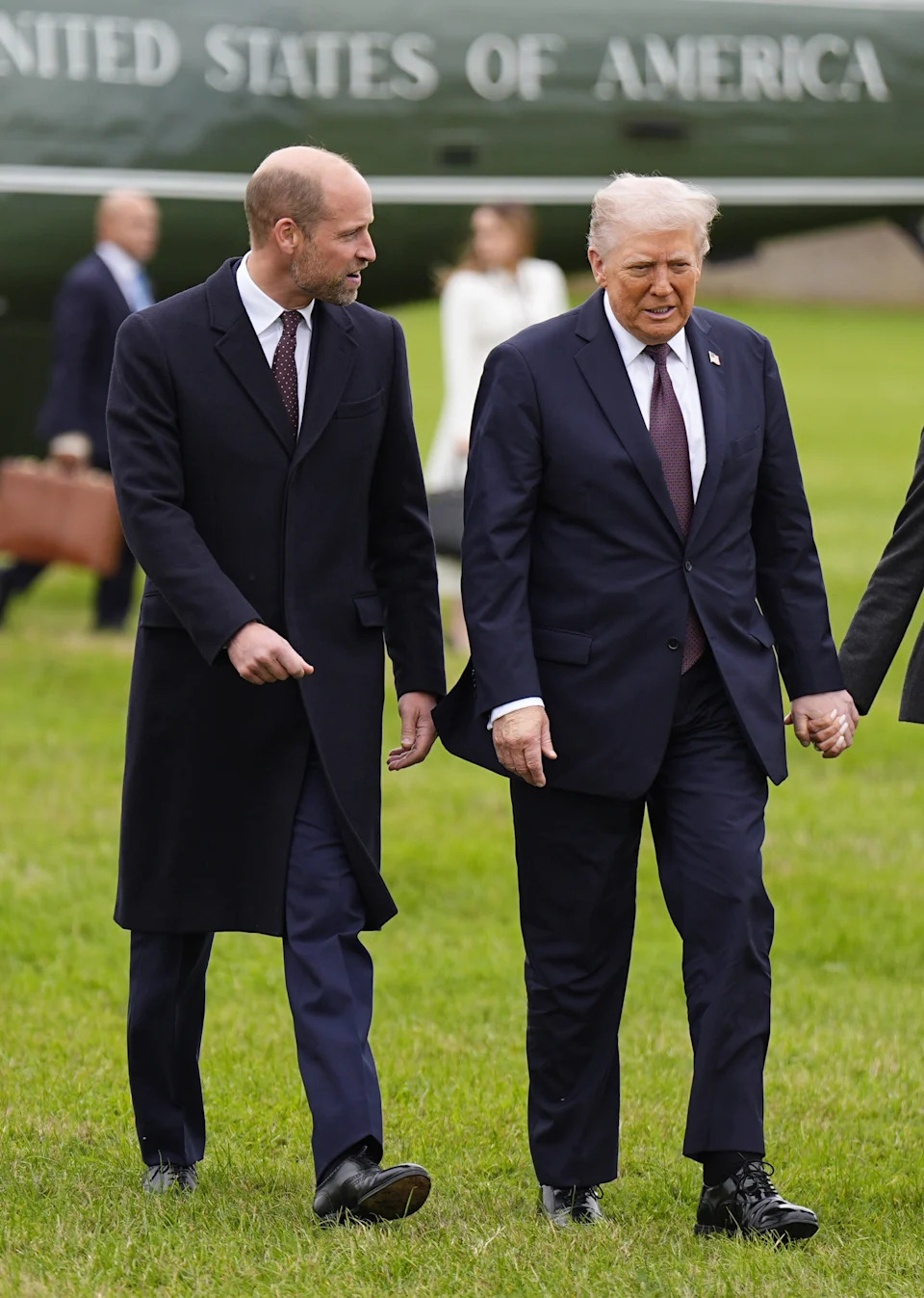 Prince William and Donald Trump walking across a field in front of a plane that says United States of America