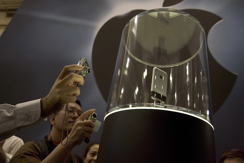 People photographing the first-generation iPhone displayed in a glass case at a tech event