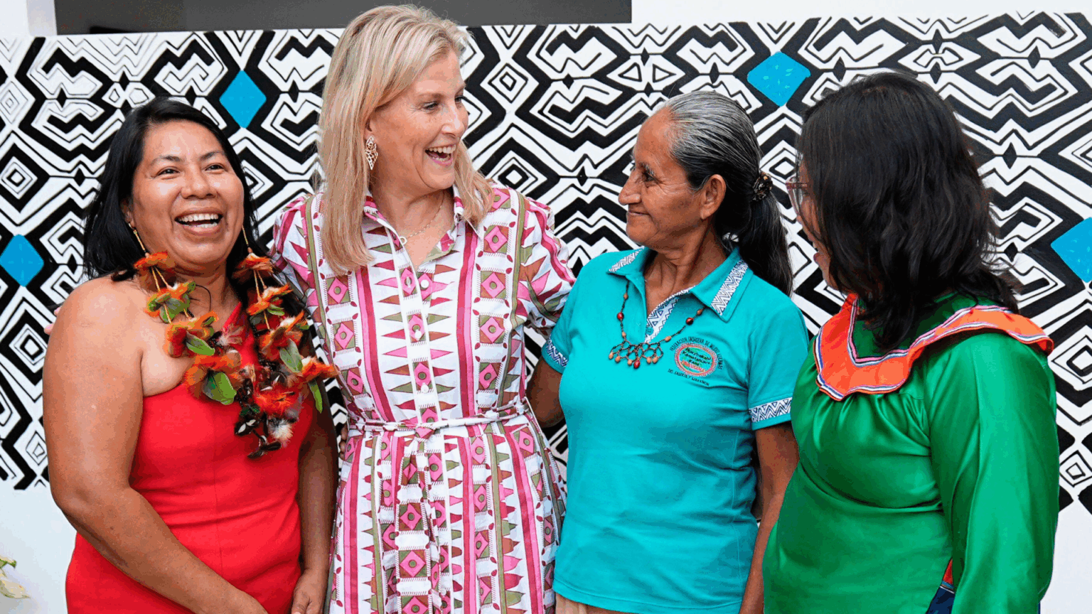 Duchess Sophie Is Following in Prince William and Princess Kate’s Footsteps as She Shows Off Her “Approachable Style” in Peru Duchess Sophie wearing a patterned shirt dress with her arms around three ladies and laughing