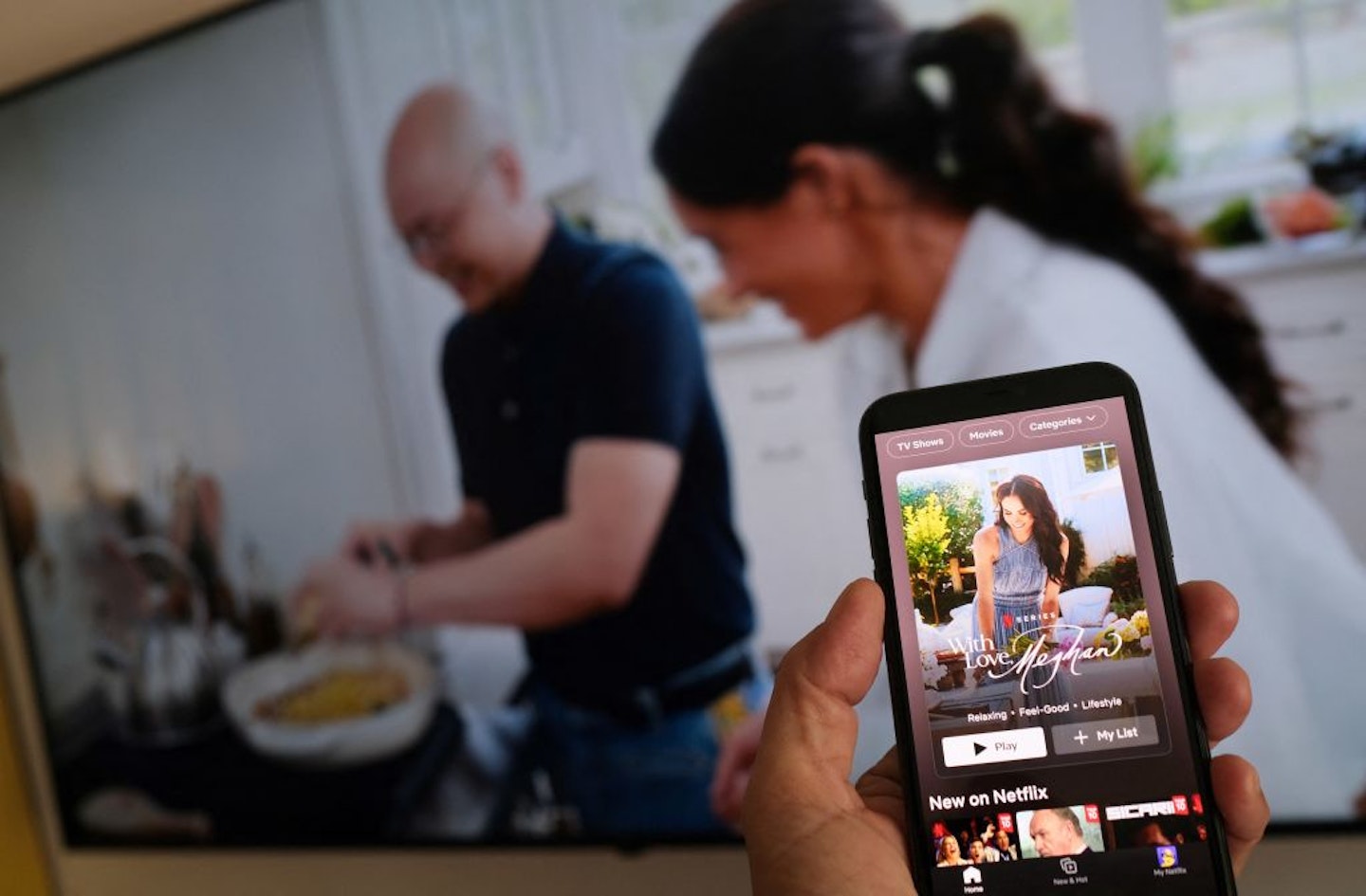 A person holds a smartphone displaying Netflix's new Meghan Markle show, "With Love, Meghan", in front of a TV screen showing footage of the show, in Los Angeles