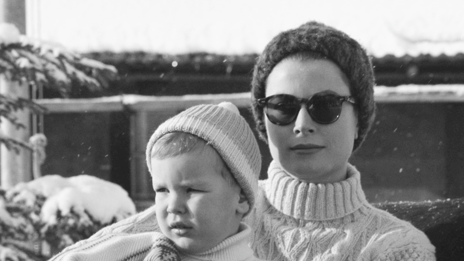 Prince Albert Says That Mom Grace Kelly “Insisted” on “Virtually Unknown” Dish Over the Holidays Grace Kelly holding young Prince Albert wearing sweaters and winter hats in front of a snowy tree
