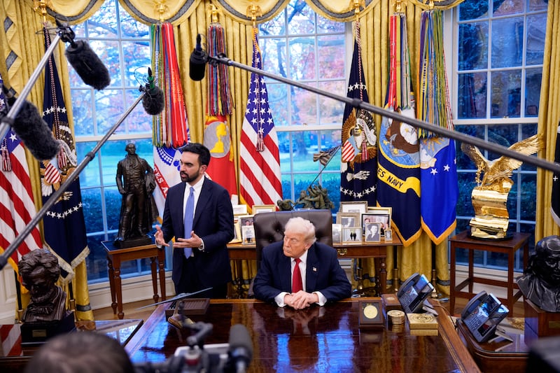 Donald Trump in the Oval Office behind his desk with microphones visible and Zohran Mamdani to the left