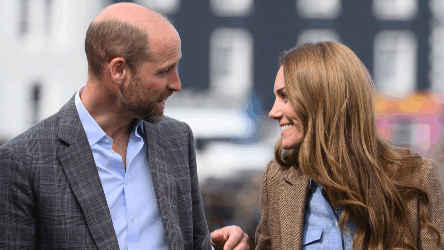 Prince William and Princess Kate “Are Happy” for the Public to See Their New “Touchy-Feely” Gestures Prince William and Kate Middleton wearing blazers and blue shirts looking at each other and smiling
