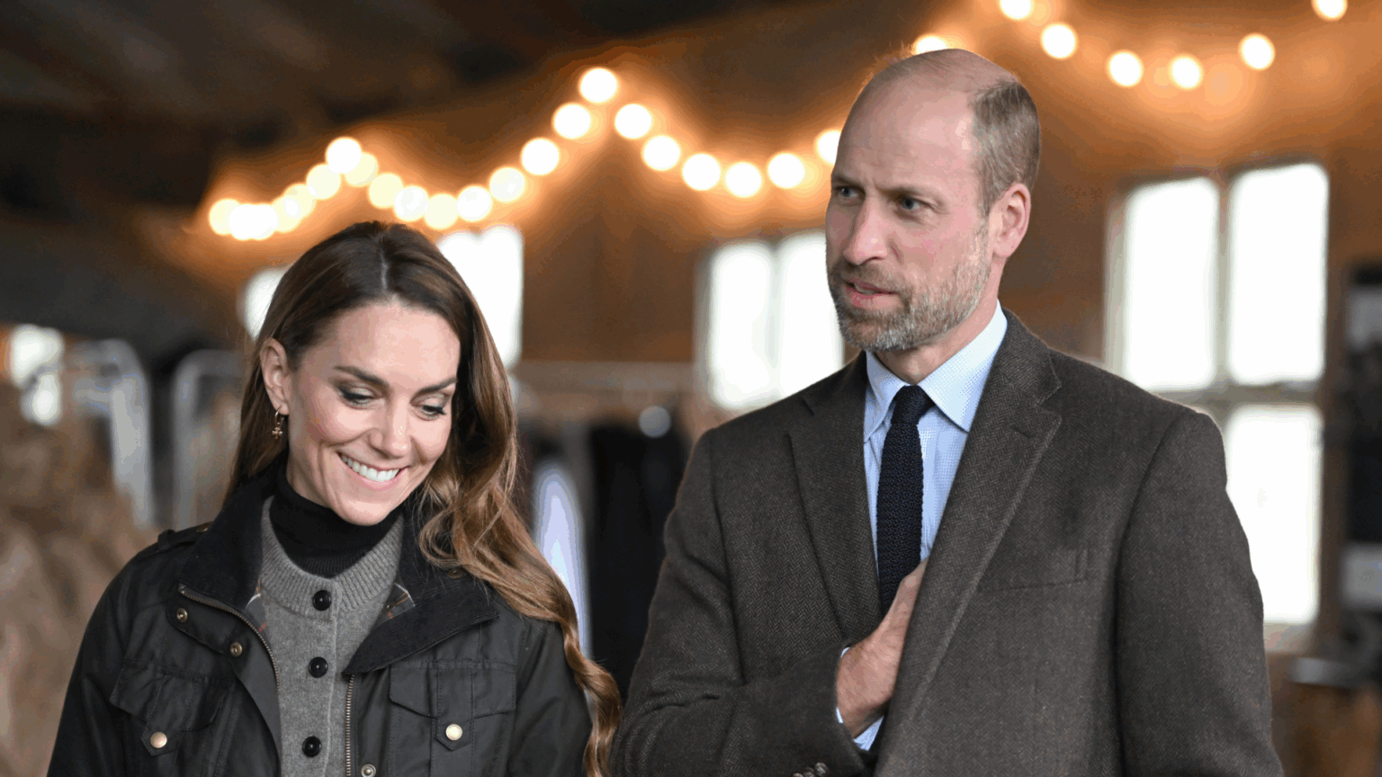 Royal Source Says Prince William Feels Like Adelaide Cottage Is “Cursed” Prince William and Princess Kate wearing brown outfits standing in front of white lights