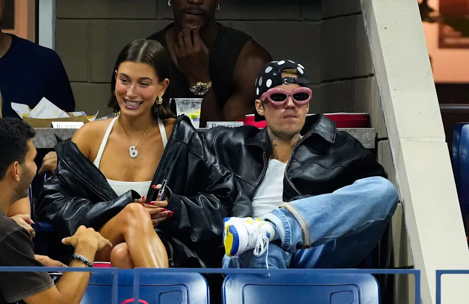 Hailey and Justin Bieber in trendy streetwear with oversized jackets and sneakers, sitting in a stadium