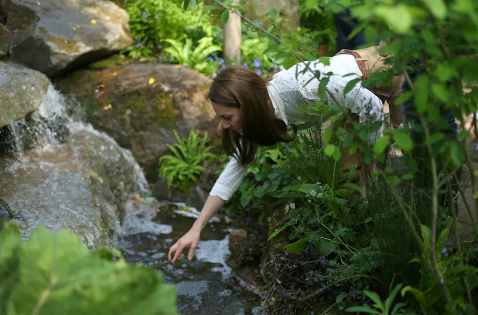 Kate Middleton wearing a white shirt leaning into a stream