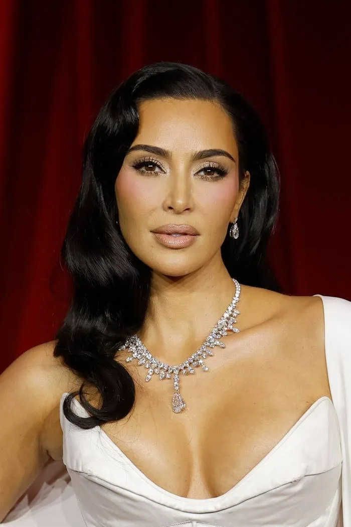 Kim Kardashian in a glamorous, elegant gown with a statement necklace, posing on a red carpet