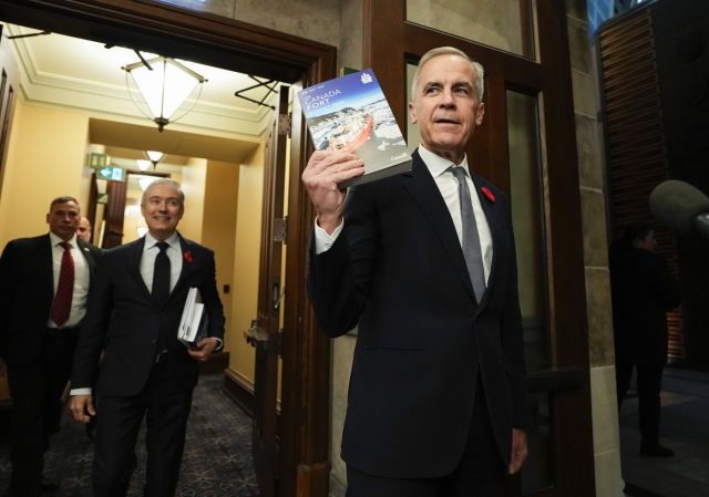 Prime Minister Mark Carney holds up a copy of the budget as he and Minister of Finance and National Revenue Francois-Philippe Champagne make their way to the House of Commons for the tabling of the federal budget on Parliament Hill in Ottawa, on Tuesday, Nov. 4, 2025. THE CANADIAN PRESS/Justin Tang