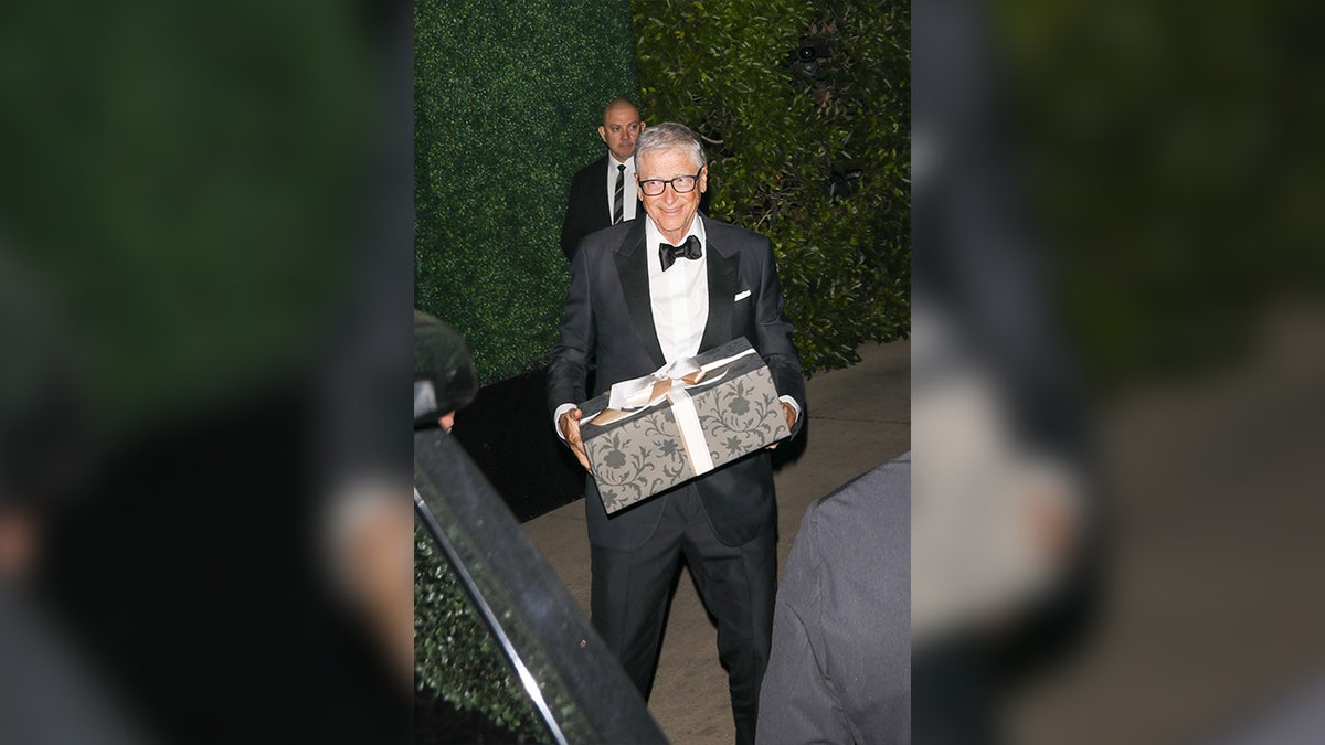 Bill Gates carries a present to Kris Jenner birthday party.