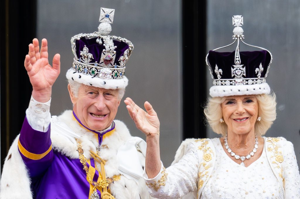 King Charles and Queen Camilla wearing crowns waving on the balcony