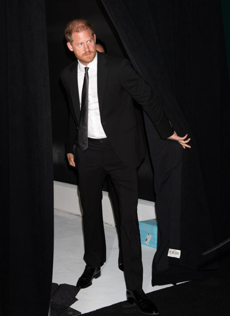 Prince Harry steps outside a black curtain