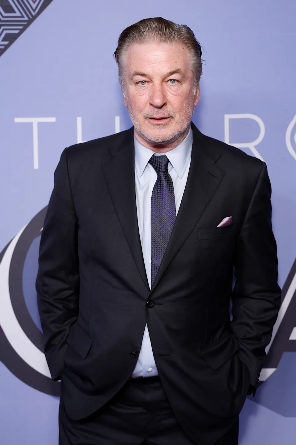 Person in a classic suit with a tie and pocket square, standing against a backdrop with abstract design