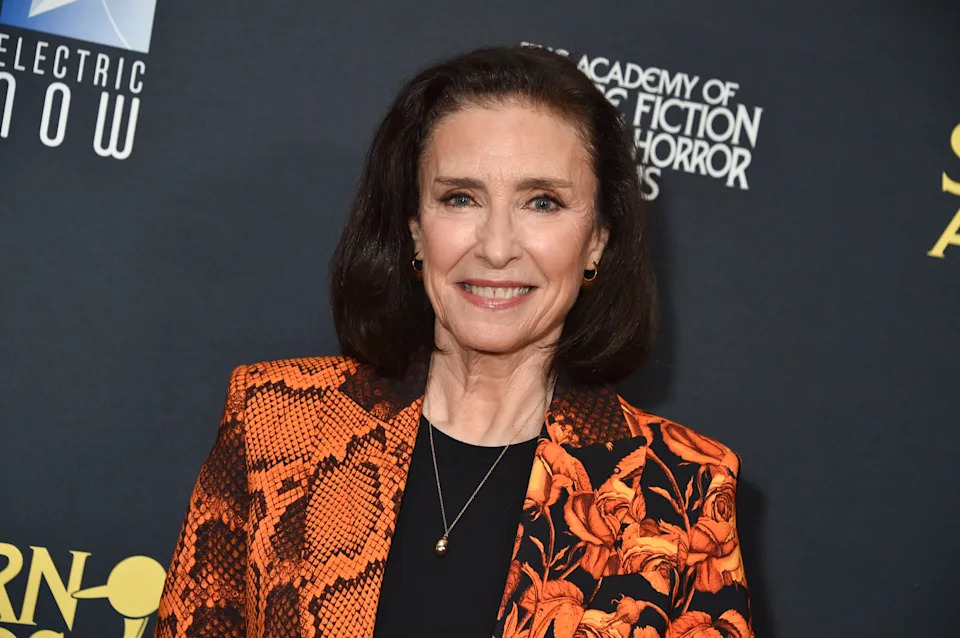 Person in patterned blazer smiles at a red carpet event. Text in the background references awards related to fiction and horror