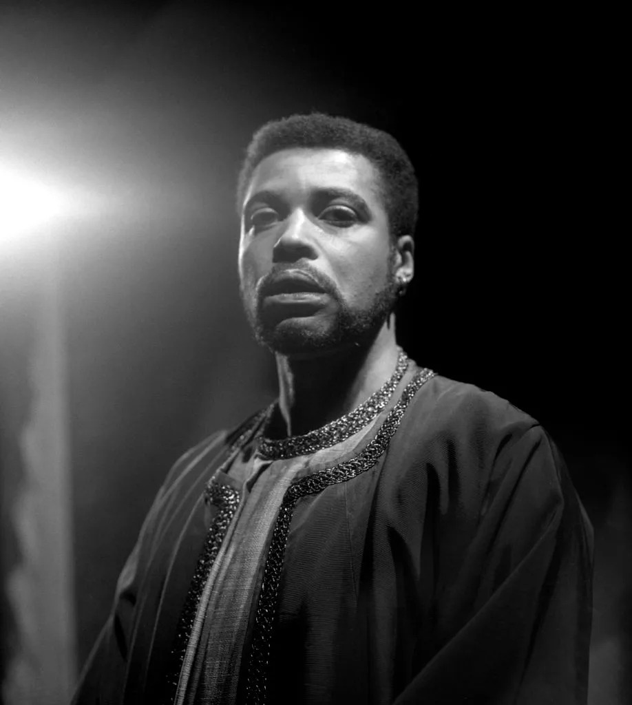 Person in long robe with decorative trim, lit dramatically from above