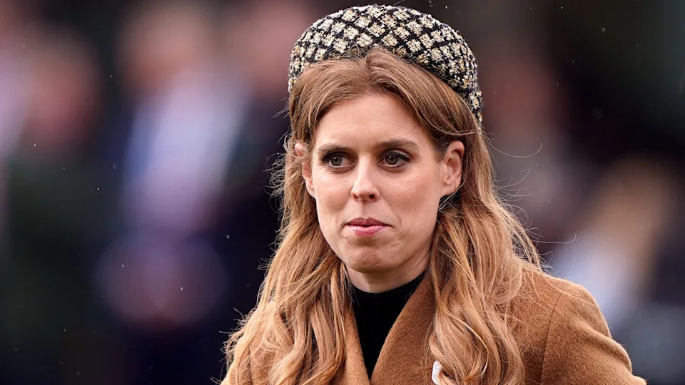 Princess Beatrice in a checkered round hat that sits upon her head and a camel colored coat