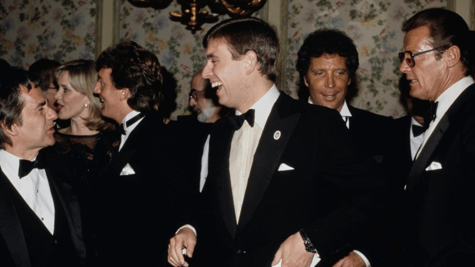 Prince Andrew in a tuxedo, laughing with Tom Jones standing behind him