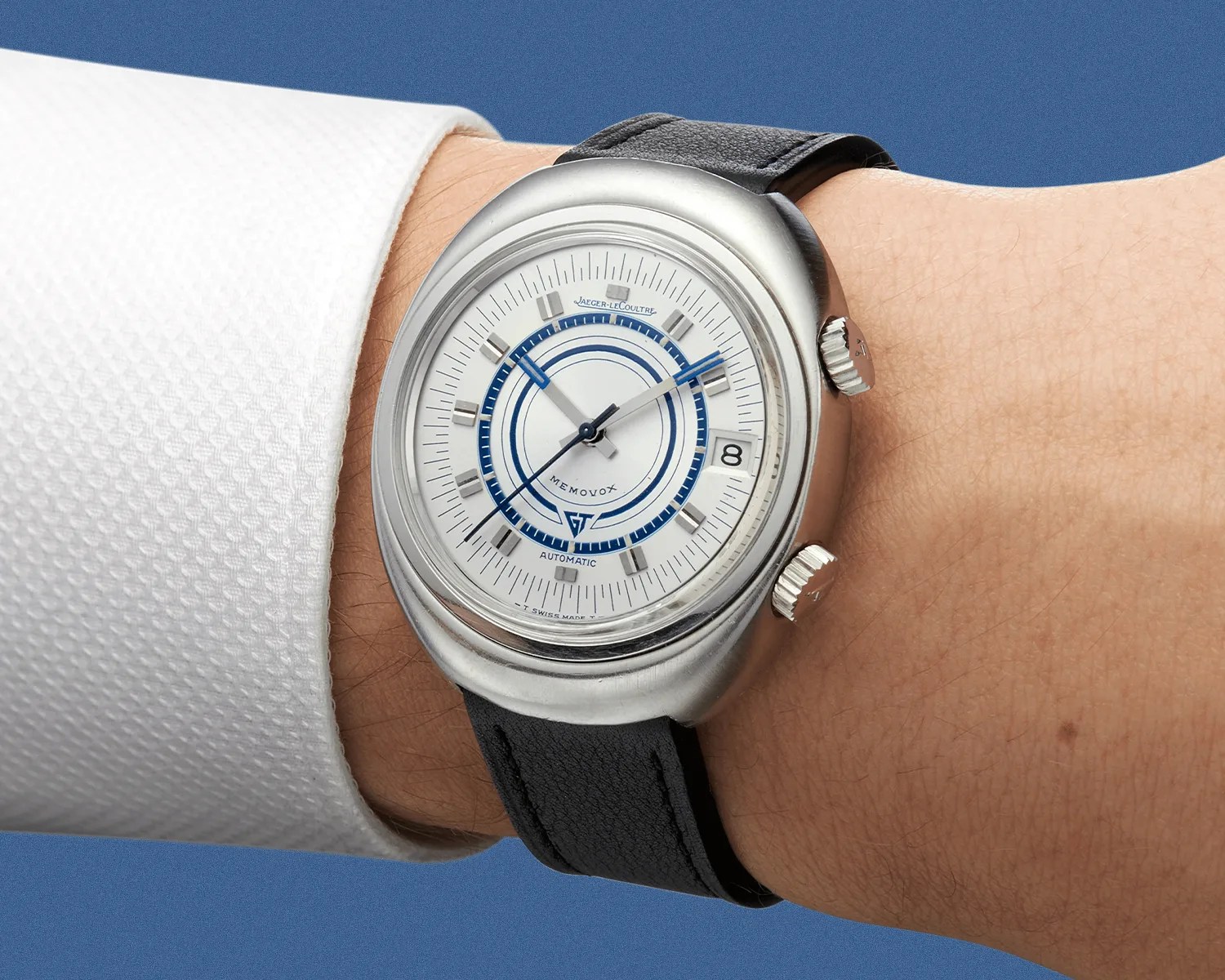Silver Jaeger-LeCoultre Memovox wristwatch with white and blue dial and black leather strap worn on a wrist.
