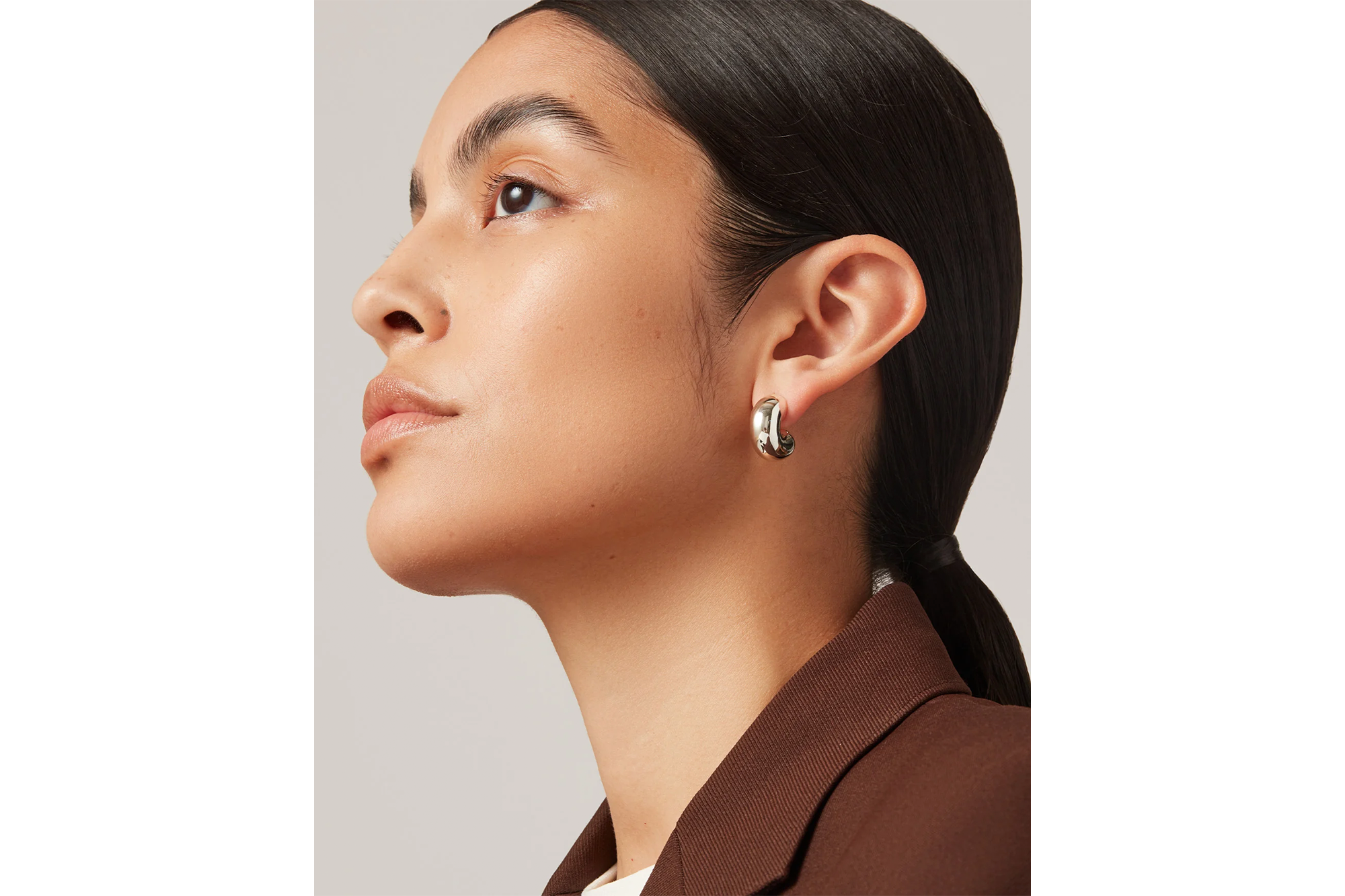 A woman with dark hair pulled back wears a single silver hoop earring.