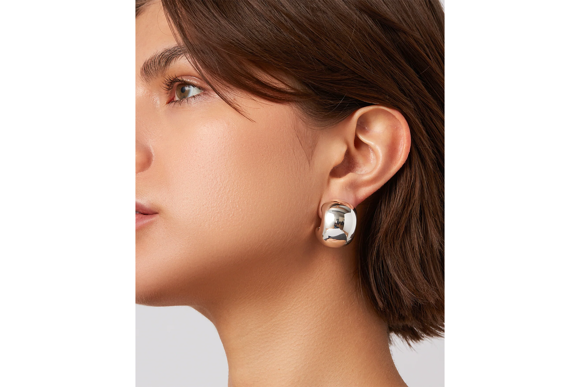Close-up of a model wearing a thick, silver, crescent-shaped earring.