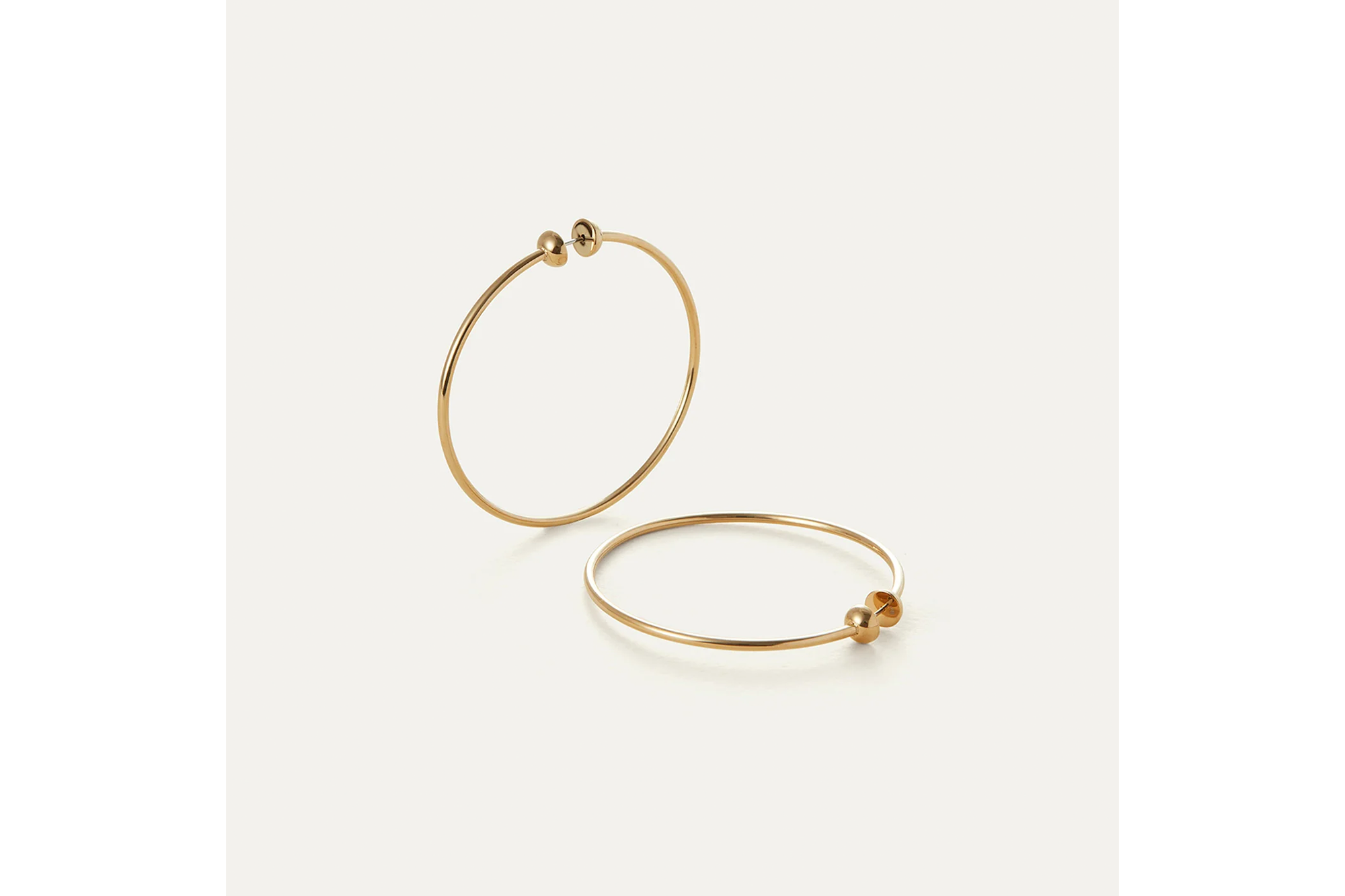 Two gold hoop earrings with small sphere details on the closures, one standing upright and the other lying flat.