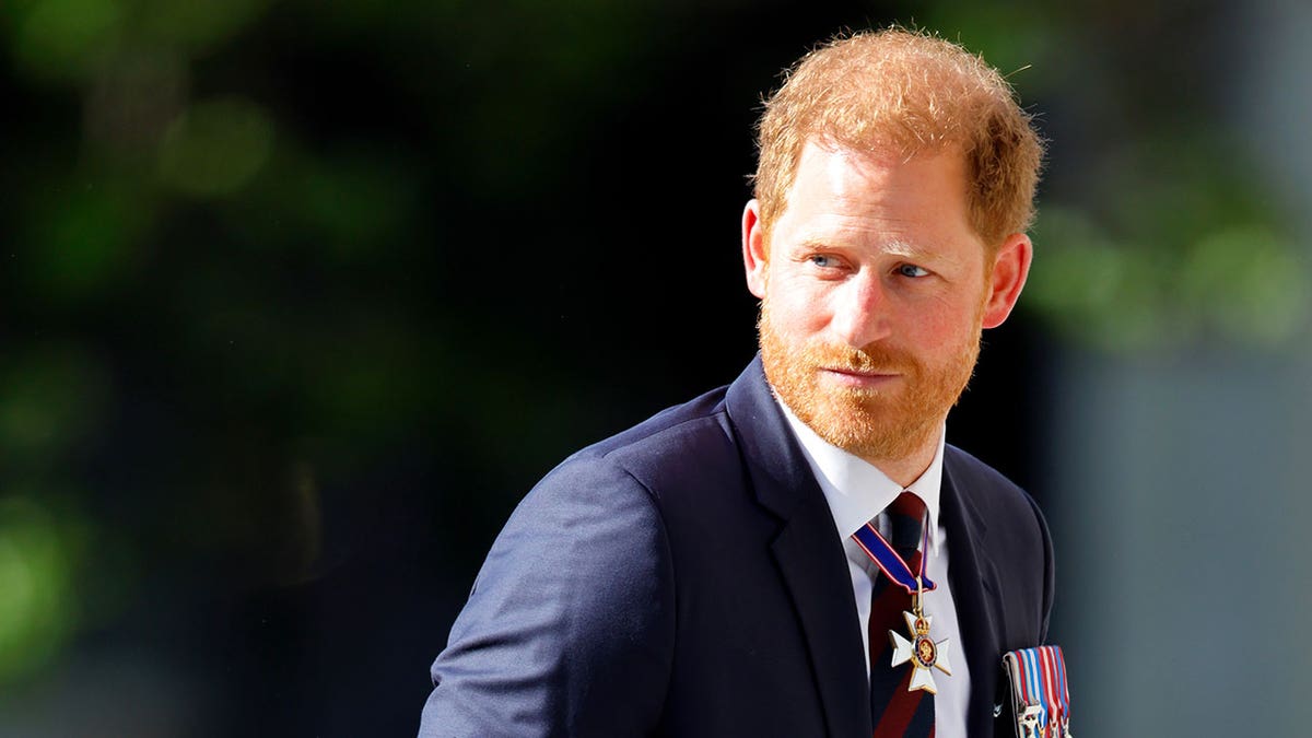 Prince Harry looking back in a dark blue suit with medals.