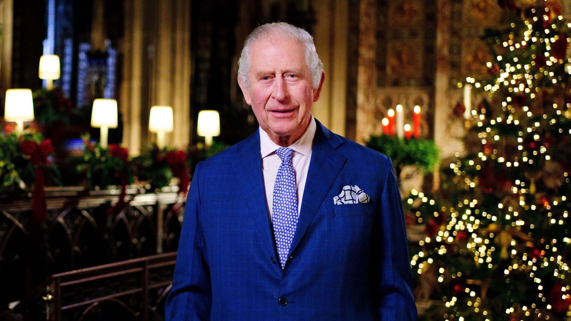 King Charles wearing a blue suit in front of a Christmas tree